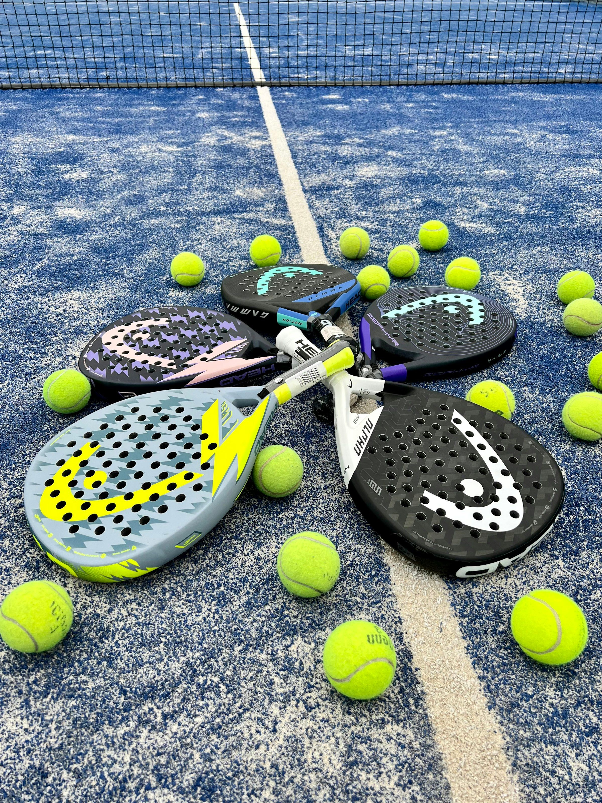 Varias palas de pádel sobre una pista azul rodeadas de pelotas